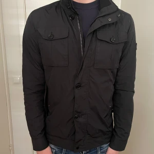 J.lindberg field jacket - Riktigt snygg j Lindberg jacka som passa perfekt för blåsigare dagar! Jackan är i bra skick förutom en knapp som lossnat vilket är enkelt fixat, förutom det finns det inga andra slitage. Modellen på bilden är 185 och väger cirka 78 kg💯🧥