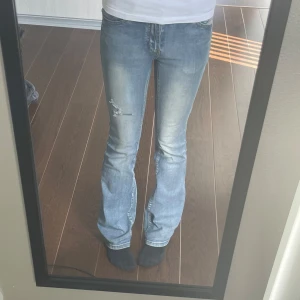 Urtvättade modell jeans - Säljer ett par blå bootcut jeans med slitningar på låret och lätt urtvättad look. Är dåligt längst ner på ena benet då de har varit för långa och jag trampar på de