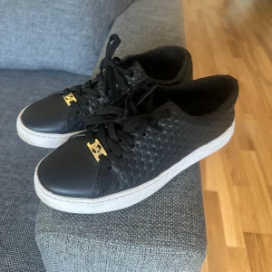 Svarta skor från Michael Kors  - Säljer ett par svarta Michael Kors sneakers köpt från Zalando, med flätad struktur på sidorna och vita sulor. Skorna har svarta snören och en snygg gulddetalj framtill med MK loggan. Endast använt 2 gånger, och säljs pga att de inte passar💕 Pris går att diskuteras!