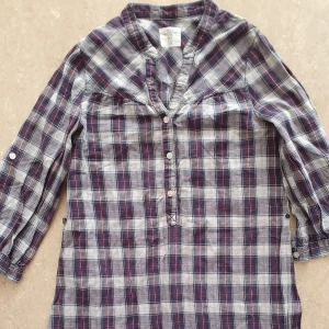 Klänning - Rutig skjortklänning i blått, vitt och rött från H&M. Klänningen har trekvartsärm, knappar framtill och volang nertill. Perfekt för en avslappnad stil med klassisk känsla.