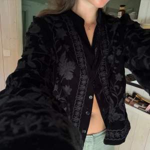Svart sammetjacka med blommigt mönster - Säljer en svart sammetjacka med broderade blommor och dekorativa detaljer. Jackan har lång ärm, knappar framtill och en elegant, lite bohemisk känsla. Perfekt för dig som vill sticka ut med en unik och stilren look. Inköpt från Zara för flera år sen och använd ett fåtal gånger, som ny! Storlek XXL men tycker den sitter bra på allt från xs-l