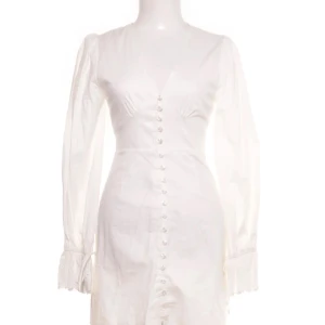 Vit klänning med knappar från Adoore - Säljer en vit kortklänning från Adoore med långa ärmar och v-ringning. Perfekt för sommaren och studenten!! (Små missfärgningar men knappt synligt!) 