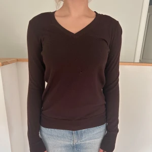 Mörkbrun v-ringad tröja - En enkel och stilren mörkbrun tröja med v-ringning och långa ärmar. Har en ganska tydlig slitning på magen, kan skicka bild vid efterfrågan, men är jätteskön och fin ändå