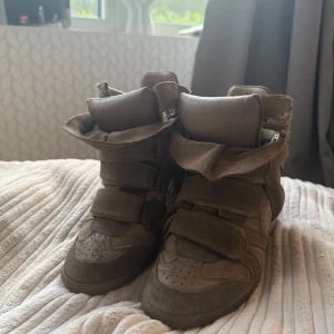 Beige sneakers med kilklack från Isabel Marant - Säljer ett par beige sneakers med kilklack från Isabel Marant. Skorna har kardborreband och är gjorda i mocka med rund tå och. Perfekta för dig som vill ha en trendig look.