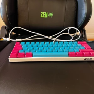 NOS Tangentbord - Ett kompakt tangentbord med färgglada blå och rosa tangenter, perfekt för dig som vill sticka ut på skrivbordet. USB-anslutning för enkel användning. Passar både gaming och studier.