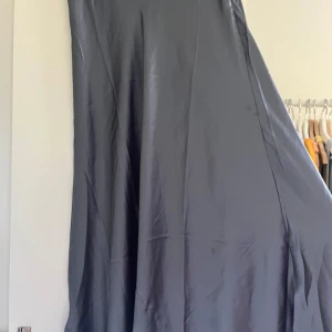 Metallic-färgad längre kjol i satin - Säljer en elegant metallicfärgad längre kjol i glansigt satinmaterial. Klänningen har en klassisk och stilren design med lång, svepande kjol. Perfekt för dig som vill ha en tidlös och sofistikerad look. Från Lager 157, i stl M. Lite volang längst ner och dold dragkedja i sidan. Använd fåtal gånger, annars mycket bra skick. Säljer då det inte är min stil längre. Kontakta gärna för mer info eller mer exakta mått. Säljer även på vinted så kontakta gärna innan tryck på ”köp”!