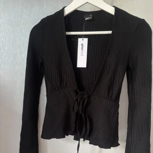 Svart Tie In Front Topp Gina Tricot - En svart ribbad ”tie in front” topp från Gina Tricot, väldigt bra skick då jag bara provat men den va för liten. Utsvängda armar och super fin till en lång kjol kanske🩷Vid snabb affär kan priset diskuteras:)