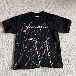 Svart t-shirt med färgstänk från Maison Margiela - Säljer denna as feta t-shirten med färgstänk från Maison Margiela! Den är i storlek M!( Lite stor i storleken!) Säljes för 400! Pris ej hugget i sten! Hör av dig vid frågor och funderingar!!