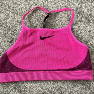 Rosa sport-bh från Nike - Säljer en rosa sport-bh från Nike med svart logga framtill. Den kan även användas för någon med storlek M och L.  Modellen har smala axelband och är tillverkad i Dri-Fit material som andas. Perfekt för träning och ger bra stöd.