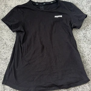 Svart t-shirt från Puma - En klassisk svart t-shirt från Puma med rund halsringning och diskret Puma-logga på bröstet. Perfekt basic-plagg som funkar till det mesta och är enkel att matcha med andra kläder.