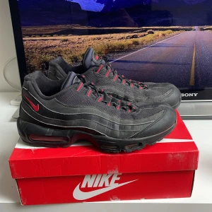 Nike Air Max 95 svart med röda detaljer - Säljer ett par Nike Air Max 95 i svart med röda detaljer och synlig Air Max-dämpning i sulan. Skorna har snörning och en sportig design med mesh och syntetmaterial. Perfekta för dig som gillar streetwear och klassiska sneakers. Storleken är 40,5 men passar mig perfekt som vanligtvis använder storlek 43
