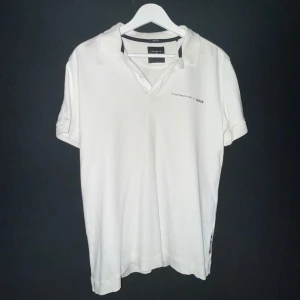 Vit piké från Porsche x Boss - Vit pikétröja från Porsche x Boss med klassisk krage och korta ärmar. Diskret logga broderad på bröstet. Perfekt för en clean och stilren look. Pikén har en normal passform och är tillverkad i bomull. Köpt på Hugo boss butik inne i NK Göteborg, hör av dig om du har några funderingar!