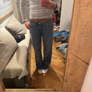 Blå raka jeansbyxor från Levis - Säljer ett par klassiska blå jeansbyxor från Levis med låg midja och raka ben. Jeansen har fem fickor och stängs med dragkedja och knapp. Perfekta till vardags för en avslappnad look.