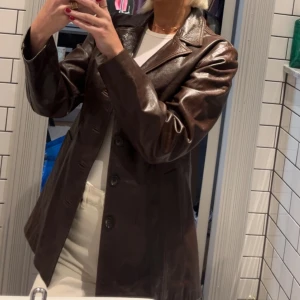 Brun skinnjacka med knappar - Bör passa dig om du har XS/S. Säljer en brun skinnjacka med klassisk krage och knäppning framtill. Jackan har lång ärm och en rak passform som ger en stilren look. Perfekt att styla över en t-shirt eller skjorta.