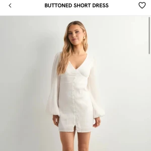 Vit kortklänning med knappar från Nelly - Kort vit klänning från Nelly med v-ringning och långa, lätt puffiga ärmar. Klänningen har knappar framtill och en feminin passform som framhäver midjan. Perfekt för sommarens tillfällen. Har aldrig använt med lappen kvar. Säljer för att den inte passade. Ny pris 499 kr säljer för 249 kr.