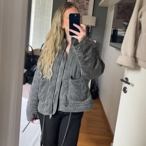 Grå quiltad jacka från Zara - Säljer en grå quiltad jacka från Zara med dragkedja och stora fickor framtill. Jackan har en oversized passform och är tillverkad i ett mjukt, strukturerat material. Perfekt för lager-på-lager och en cool vardagslook. Defekt syns på bild!
