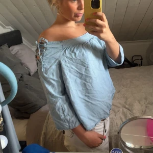 Ljusblå offshoulder blus med snörning - Säljer en ljusblå offshoulder blus med snörningsdetaljer på axlarna. Blusen har trekvartsärm och en lös passform, perfekt för vår och sommar. (Köpt för 400kr på vinted)