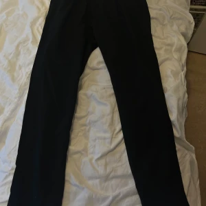 Svarta byxor från Elvine Isaacson - Säljer ett par svarta byxor från Elvine, modell Isaacson. Byxorna har en klassisk rak passform och är tillverkade i ett slätt material. Perfekta för en stilren look. Prislappen är kvar och de kostade 999kr 