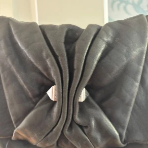 Svart axelväska med rosett och mönstrat foder - Säljer en svart axelväska i skinn med stor rosettdetalj på framsidan. Insidan har ett unikt foder med röda stjärnor och blixtar på svart bakgrund. Väskan knäpps med magnet och passar perfekt för dig som vill ha något coolt och annorlunda.