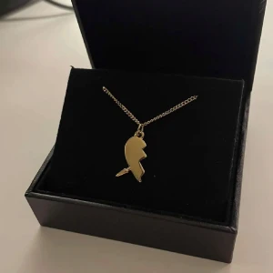 Maria Nilsdotter inspirerat halsband  - Säljer ett stilrent halsband i guld med en unik, modern berlock som påminner om ett citattecken. Kedjan är tunn och elegant, perfekt för att lyfta din outfit. Levereras i en snygg svart ask.