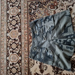 Camouflage shorts med fickor - Säljer ett par klassiska camouflage shorts med flera praktiska fickor och knappstängning. Perfekta för dig som gillar en avslappnad och cool stil. Mjukt och slitstarkt material.