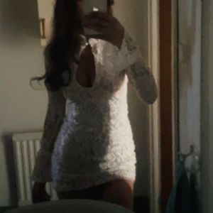 Vit spetsklänning med lång ärm - Kort vit klänning med lång ärm och djup v-ringning. Klänningen är täckt av spets och har en figurnära passform. Perfekt för dig som vill sticka ut med en elegant och feminin look.