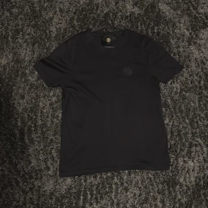 Svart t-shirt från Limitato - Säljer en stilren svart t-shirt från Limitato med broderad logga på bröstet. Klassisk passform och rund halsringning, perfekt till vardags. Materialet känns mjukt och bekvämt.