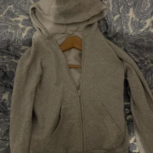 Grå hoodie från H&M - Säljer en enkel och stilren grå hoodie från H&M i storlek 146/152. Tröjan har dragkedja framtill, huva och två fickor. Perfekt för en avslappnad look och passar året runt.