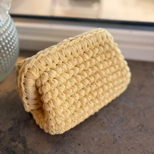 Gul virkad necessär  - Säljer en söt gul handväska som är virkad i ett tjockt garn. Väskan har en mjuk och fluffig känsla med rektangulär form och stängs upptill. Perfekt accessoar för att liva upp din outfit! Kika gärna in vår Instagram @design.by.bela för andra necessärer och väskor. Du kan även designa din egna väska utifrån din favoritfärg. 