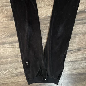 Svarta velourbyxor från Juicy Couture - Svarta mjukisbyxor i velour från Juicy Couture med strassdetaljer och texten 'Juicy' på baksidan. Byxorna har dragsko i midjan och muddar vid bensluten. Perfekta för en avslappnad och trendig look. Dom är knappt använda. OBS! Original storlek på dessa är XXS men dom är uppsydda. På sista bilden ser ni hur dom sitter på mig, jag är ungefär 145 cm tror jag men dom går säkert att sprätta upp (är inte säker) men valde att inte göra det💓💓Jag kan skicka bättre och noggrannare bilder vid intresse!