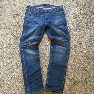 Blå jeansbyxor från Lee - Säljer ett par klassiska blå jeans från Lee med raka ben och normal passform. Byxorna har fem fickor, gylf med dragkedja och knapp samt tydliga sömmar. Perfekta för dig som gillar tidlös denimstil. 34w 34l