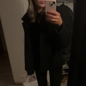 Svart jacka från Monki - Snygg svart jacka från Monki med knappar framtill och stora fickor. Jackan är använd en höst/vinter därefter har den blivit ”nopprig” i tyget, det går sjävklart att ta bort dock inget jag har prioriterat då jag inte använder jackan dagligen annars är den i fint skick 🤗