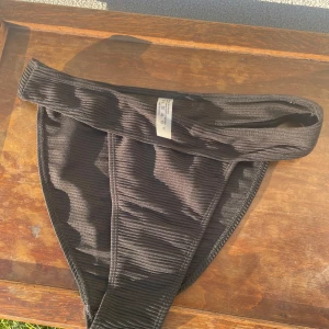 Svart ribbad bikiniunderdel - Säljer en svart bikiniunderdel i ribbat material. Modellen har hög midja och breda sidor för en bekväm passform. Perfekt för strand eller poolhäng i sommar!