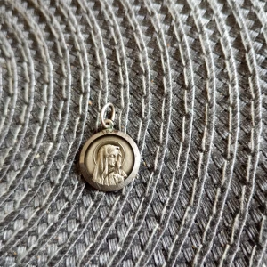 Rund silverberlock med religiöst motiv - Säljer en rund berlock i silver med ett detaljerat motiv av en kvinna med slöja, troligen Jungfru Maria. Berlocken har en ögla för kedja och är stämplad 925 på baksidan.