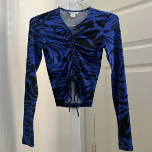 Blå och svart långärmad topp från Monki - Säljer en blå och svart långärmad topp från Monki med zebramönster och snörning framtill. Modellen är tight och croppad, perfekt för att sticka ut med ett coolt mönster. Materialet är stretchigt och bekvämt.💙