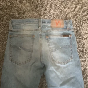 Ljusblå skinny jeans från Nudie Jeans - Säljer ett par ljusblå jeans från Nudie Jeans. Klassisk femficksmodell med orange sömmar och läderpatch bak i midjan. Jeansen har en smal passform och är tillverkade i mjukt denimtyg.