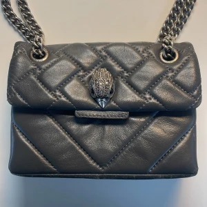 Grå väska från Kurt Geiger - Snygg väska från Kurt Geiger med kedjerem, går att ha på axeln och som vanligt. Några defekter. Perfekt för att lyfta din outfit med en lyxig touch. Medföljer en dustbag!