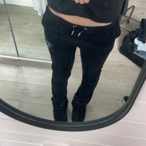 Svarta mjukisbyxor med strasstenar från juicy couture - Svarta mjukisbyxor med glittrande strasstenar på ena benet och snörning i midjan. Byxorna har normal passform och är perfekta för en avslappnad stil. Mjukt material och bekväma fickor på sidorna.