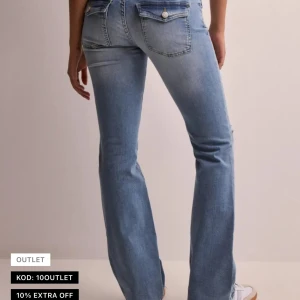 Low waist bootcut flap pocket jeans - Säljer ett par lågmidjade ljusblå jeans med bootcut passform och hål vid knäna. Jeansen har klassiska bakfickor med lock och knapp. Perfekta för en avslappnad och trendig look. Säljer då dom ej kommer till användning. Använda en gång, skriv om ni vill ha mer bilder💕