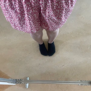 Rosa blommiga shorts med resårmidja - Säljer ett par rosa shorts med vitt blommönster och resår i midjan. De har en lös passform och är tillverkade i ett mjukt, tunt bomullstyg. Perfekta för varma dagar och ger en avslappnad känsla. Det är en kjol fast som shorts i.