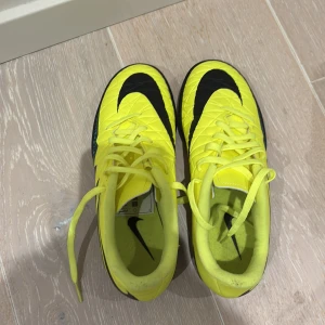 Gula Nike fotbollsskor med svart mönster - Säljer ett par gula Nike fotbollsskor med svart sula och stora svarta Nike-loggor. Skorna har snörning och ett coolt grafiskt mönster i svart och turkos på sidorna. 