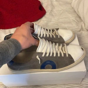 Grå sneakers med blå detalj från Oliver cabell  - Säljer ett par grå sneakers från Oliver cabell med vita snören, vit sula och blå detalj på hälen samt sidan. 