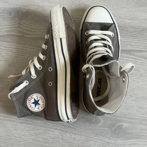 Grå Converse Chuck Taylor All Star - Säljer ett par klassiska grå Converse Chuck Taylor All Star high-tops med vita snören och gummisula. Skorna har rund tå, vit tåhätta och Converse-logga på sidan. Knappt använda köptes för ca 800 kr. Storlek 36,5, passar mig perfekt som brukar ha 37/38☺️