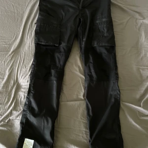 Svarta cargopants från Top Swede - Säljer ett par svarta cargopants från Top Swede med flera praktiska fickor på benen. Perfekta för dig som gillar funktionella byxor med lite mer plats för prylar. Klassisk passform och tåligt material.