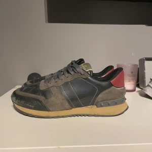 INTRESSEKOLL Valentino rockrunners - Säljer ett par Valentino Rockrunner sneakers med grå mocka, svarta och blå detaljer samt röd häl. Skorna har snörning och en platt sula med mönster. Perfekta för dig som gillar exklusiva och stilrena sneakers. Det är en intresse koll kom gärna med prisförslag. Allt og finns med men kunde ej ta kort på det då det ligger hos min mamma. 