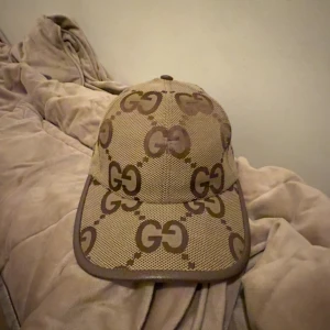 Beige keps från Gucci med GG-mönster - helt ny oanvänd kommer med dustbag möts upp i göteborg men tar hellre byten än att sälja har du andra gucci kepsar tar även byten kepsen är i storlek (M) inga skador på kepsar