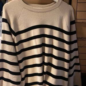 Randig beige och svart stickad tröja - Säljer en beige stickad tröja med svarta horisontella ränder. Tröjan har rund halsringning och långa ärmar. Perfekt för en avslappnad och stilren look.