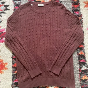 Brun kabelstickad tröja Selected Homme - Snygg brun kabelstickad tröja från Selected Homme i storlek S. Tröjan har rund hals, ribbade muddar och ett klassiskt kabelmönster över hela plagget. Perfekt för dig som gillar stilrena och tidlösa plagg med lite extra struktur.