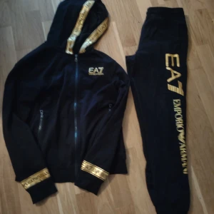  EA7 Emporio Armani Set - Ett set med byxa och tröja med dragkedja i svart och guld. Tröja i storlek S och byxor i storlek M, setet har använts tillsammans men byxorna har använts mer och är lite tvättblekta