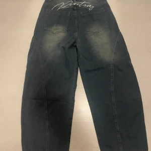  jeans med broderi - Säljer ett par wide jeans med coola slitningar framtill och broderad text' på bakfickan. Jeansen har klassiska fem fickor. Materialet är jeans och passformen är loose för en avslappnad vibe.